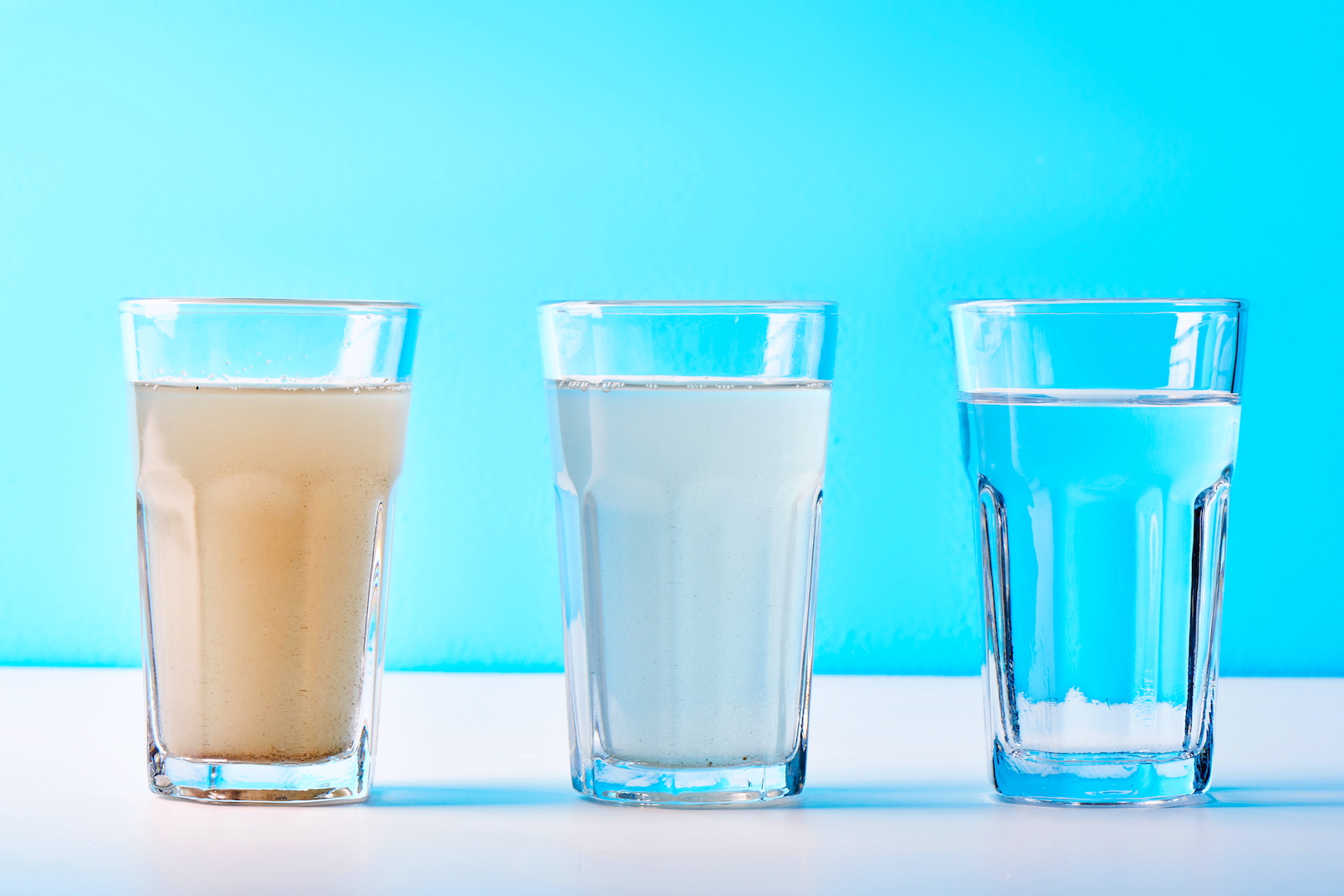 Three glasses of water starting out dirty on the left side and progressively getting cleaner in water quality