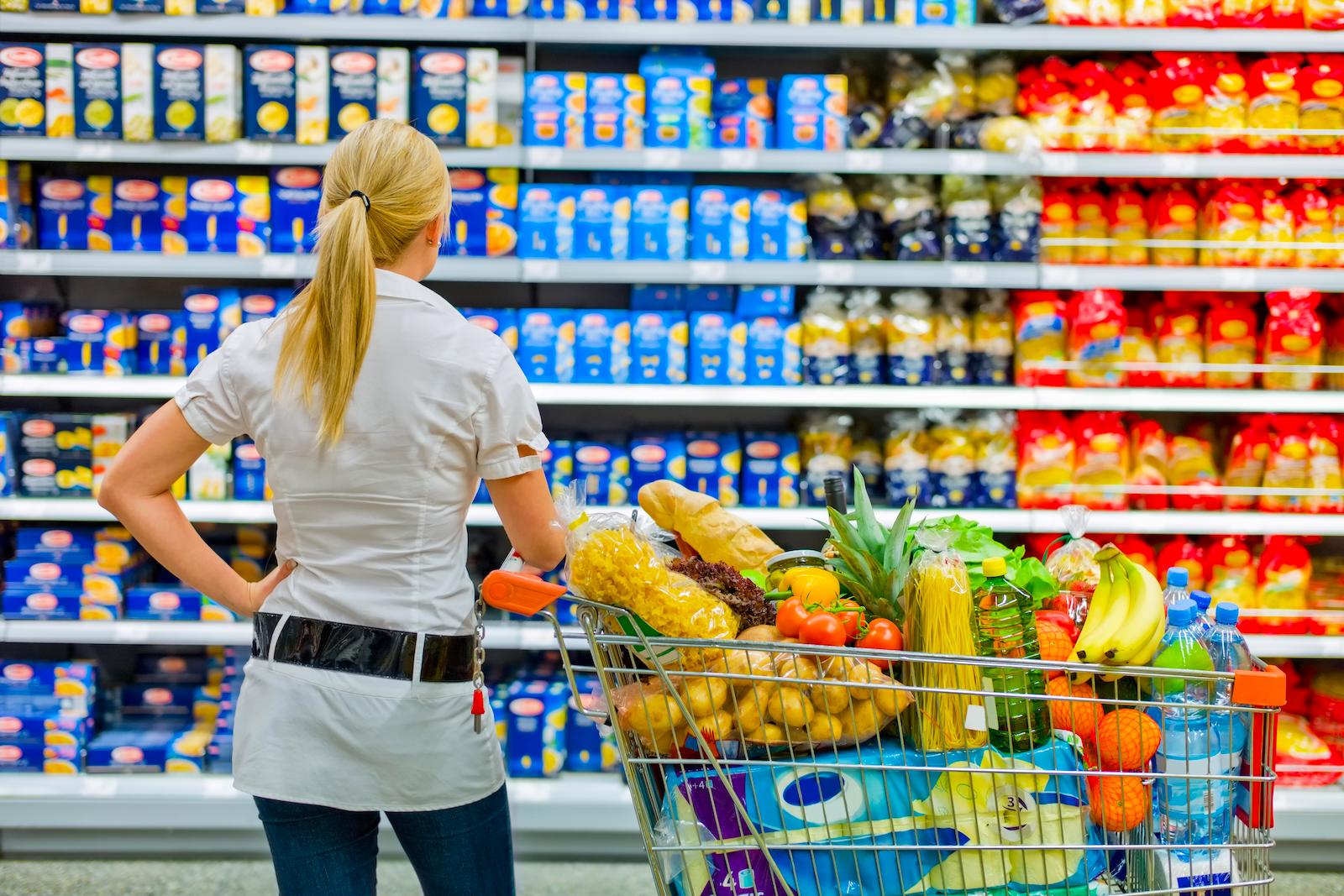 Woman next to a full shopping cart looking at grocery store shelves
