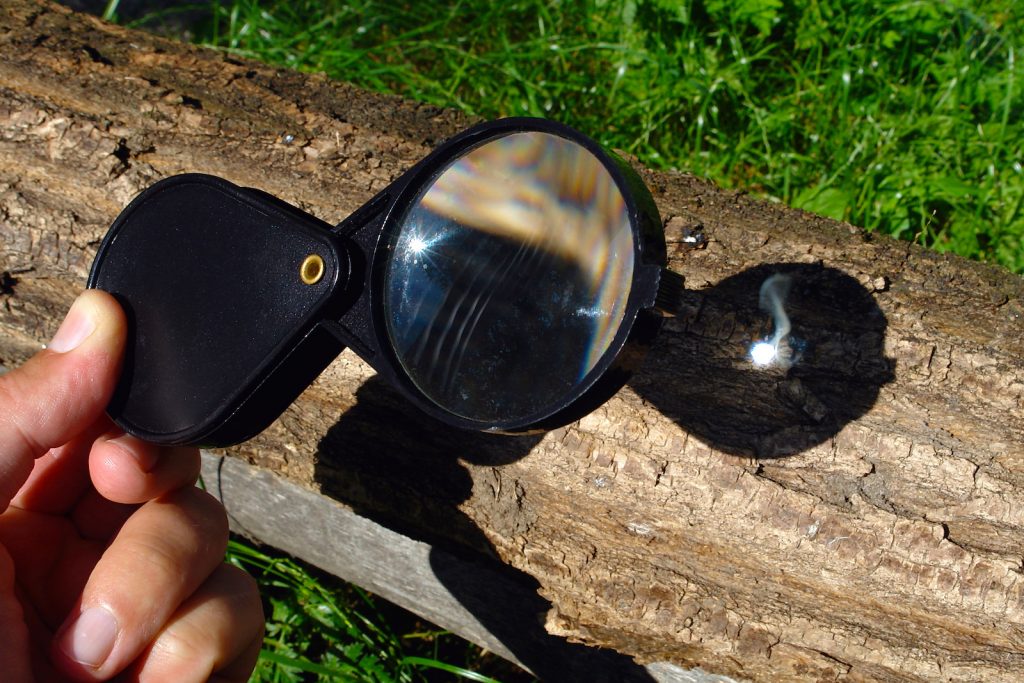 Magnifying glass reflecting the sun to start a fire on a log