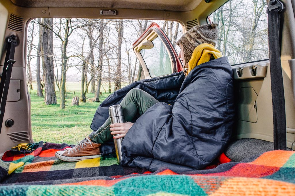 woman wearing a sleeping bag living in a vehicle