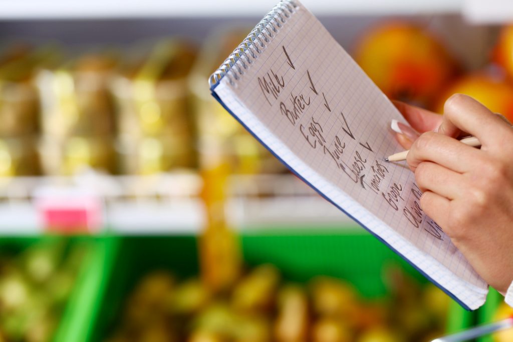 Shopping list with groceries on it while rows of food are in the background
