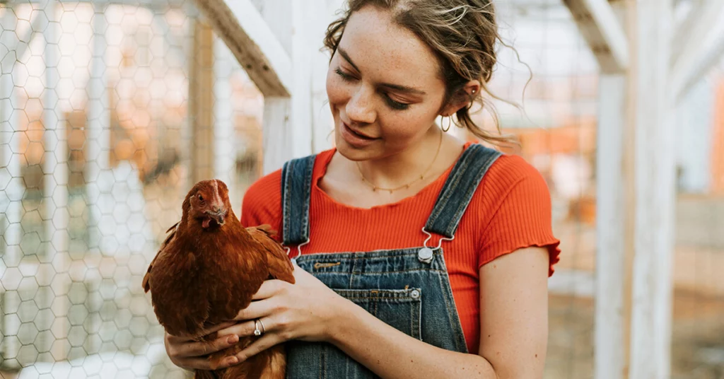 woman in a red shirt and overalls holding a chicken